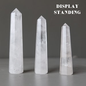 May include: Three clear quartz crystal points of varying sizes standing upright on a gray surface. The text "DISPLAY STANDING" is visible at the top of the image.