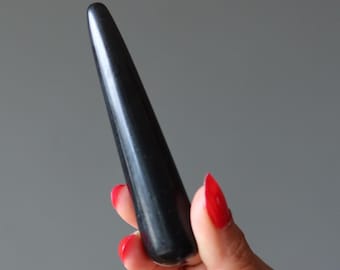 May include: A smooth, black, elongated object with a tapered end. The object is held in a hand with red nail polish. The item has a glossy finish and appears to be made of a solid, dark material.