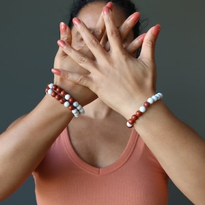 May include: Two bracelets on a person's wrist. One bracelet is made of red and white beads, and the other is made of white and red beads.