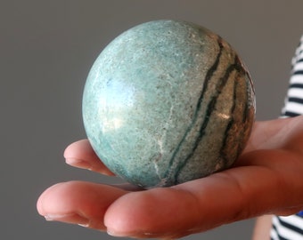 May include: A smooth, green and black marble sphere with swirling patterns.