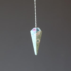 May include: A green and pink crystal pendulum with a silver chain. The crystal is faceted and has a pointed tip.