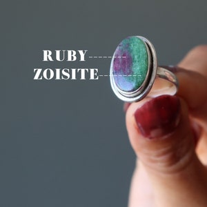 May include: A silver ring with a green and pink oval gemstone. The gemstone is labeled "RUBY" and "ZOISITE".