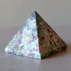 May include: A green, pink, and white pyramid-shaped crystal. The crystal has a speckled appearance with a variety of colors and textures.