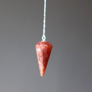 May include: A red crystal pendulum on a silver chain. The crystal is faceted and has a pointed tip.
