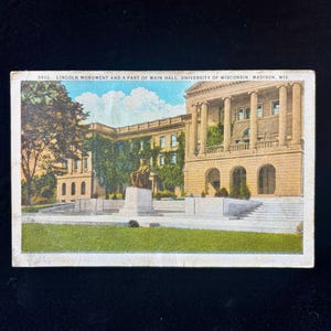 Op de afbeelding: Vintage ansichtkaart met het Lincoln Monument en een deel van Main Hall, University of Wisconsin, Madison. De afbeelding toont een klassiek gebouw met zuilen, een standbeeld en groen. De tekst "3602. LINCOLN MONUMENT AND A PART OF MAIN HALL, UNIVERSITY OF WISCONSIN, MADISON, WIS." staat bovenaan.