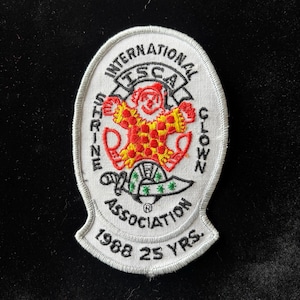 May include: Embroidered patch featuring a clown with a red and yellow outfit, surrounded by text. The patch reads "International Shrine Clown Association" and "1988 25 YRS."