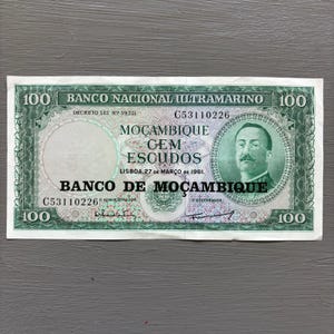May include: A vintage 100 Escudos banknote from Banco de Moçambique, featuring a portrait of a man on the right and intricate green and purple designs. The text includes "Banco Nacional Ultramarino" and "Moçambique".