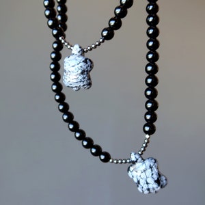 Può includere: Una collana di perline nere con due ciondoli a motivi bianco e nero. La collana è composta da perline rotonde e i ciondoli hanno la forma di una tartaruga.