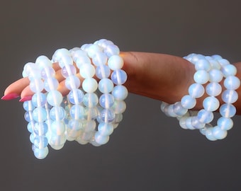 Könnte beinhalten: Ein weißes Opal-Perlenarmband mit irisierendem Schimmer. Das Armband besteht aus runden Perlen und ist um eine Hand gelegt.