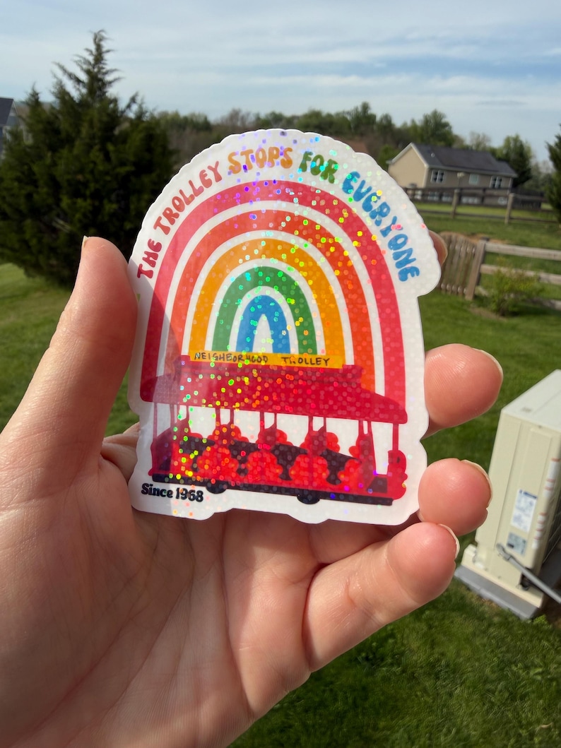May include: A vibrant sticker with a rainbow design and the words "THE TROLLEY STOPS FOR EVERYONE." A red trolley car is depicted below the rainbow. The sticker also includes the text "NEIGHBORHOOD TROLLEY" and "Since 1968."