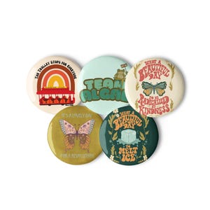 May include: Five circular pinback buttons featuring colorful graphic designs. One shows a red trolley and rainbow with text, another a frog with text, one a butterfly with text, one a butterfly with text, and one an ice cube with text.