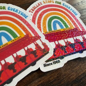 May include: Two stickers showing a red trolley design with a rainbow arch and the text "Trolley Stops For Everyone" and "Since 1968". The stickers have a glittery finish.