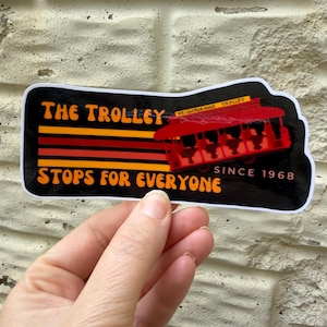 Puede incluir: Una pegatina con un tranv&iacute;a rojo y el texto "THE TROLLEY STOPS FOR EVERYONE SINCE 1968". La pegatina tiene un fondo negro con rayas y texto naranja y rojo.