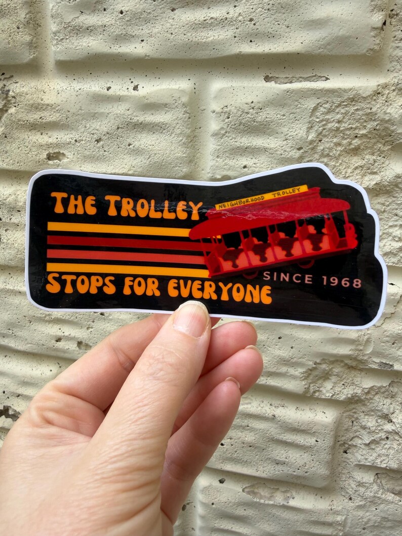 Puede incluir: Una pegatina con un tranv&iacute;a rojo y el texto "THE TROLLEY STOPS FOR EVERYONE SINCE 1968". La pegatina tiene un fondo negro con rayas y texto naranja y rojo.