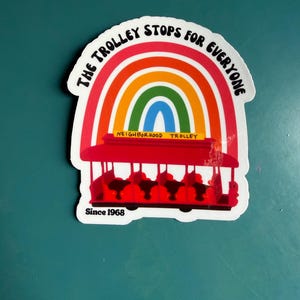 Pu&ograve; includere: Un adesivo raffigurante un tram rosso con un arcobaleno sopra. Il testo "THE TROLLEY STOPS FOR EVERYONE" &egrave; arcuato sopra l'arcobaleno. Le parole "NEIGHBORHOOD TROLLEY" sono sotto, e "Since 1968" in basso.