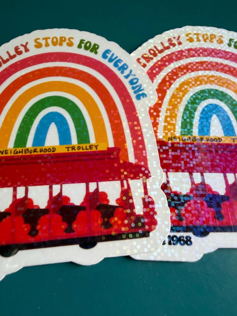 May include: Two stickers featuring a rainbow design and a red trolley. The stickers display the text "Trolley Stops for Everyone" and "Neighborhood Trolley". One sticker has the year "1968". The stickers have a glittery finish.