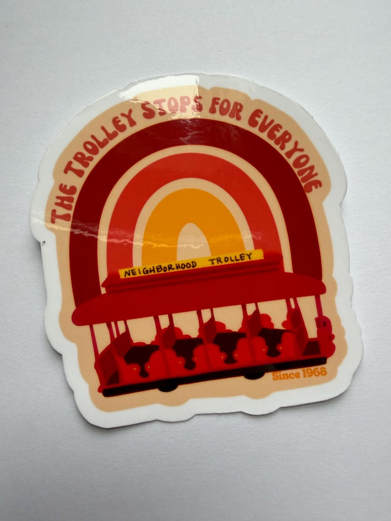 May include: A sticker featuring a red trolley with the text "THE TROLLEY STOPS FOR EVERYONE" in a semi-circular design. The trolley is set against a rainbow background with the words "NEIGHBORHOOD TROLLEY" and "Since 1968".