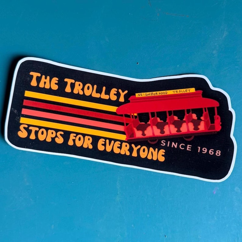 Puede incluir: Una pegatina con fondo negro y las palabras "THE TROLLEY STOPS FOR EVERYONE" en naranja. Un gr&aacute;fico de tranv&iacute;a rojo a la derecha, con el texto "NEIGHBORHOOD TROLLEY" encima. La pegatina tambi&eacute;n dice "SINCE 1968".