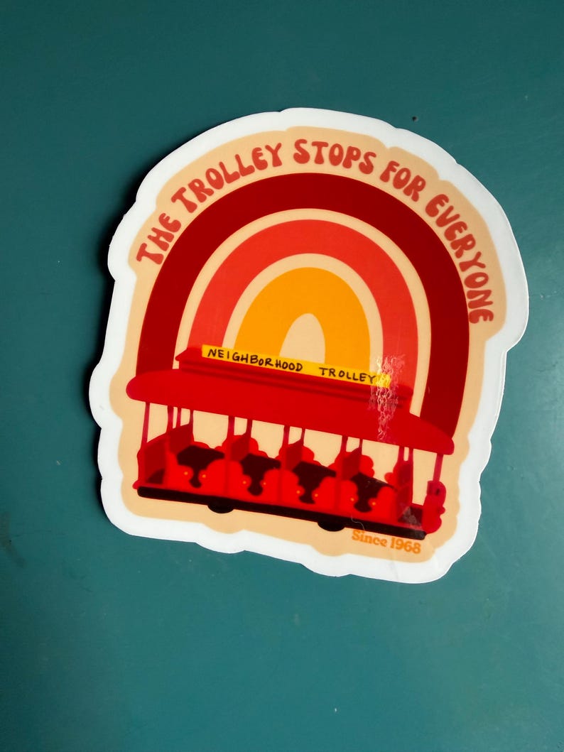 May include: A sticker featuring a red trolley with a rainbow design in shades of red, orange, and yellow. The text "THE TROLLEY STOPS FOR EVERYONE" arches above the trolley. The words "NEIGHBORHOOD TROLLEY" are on the trolley, and "Since 1968" is at the bottom.