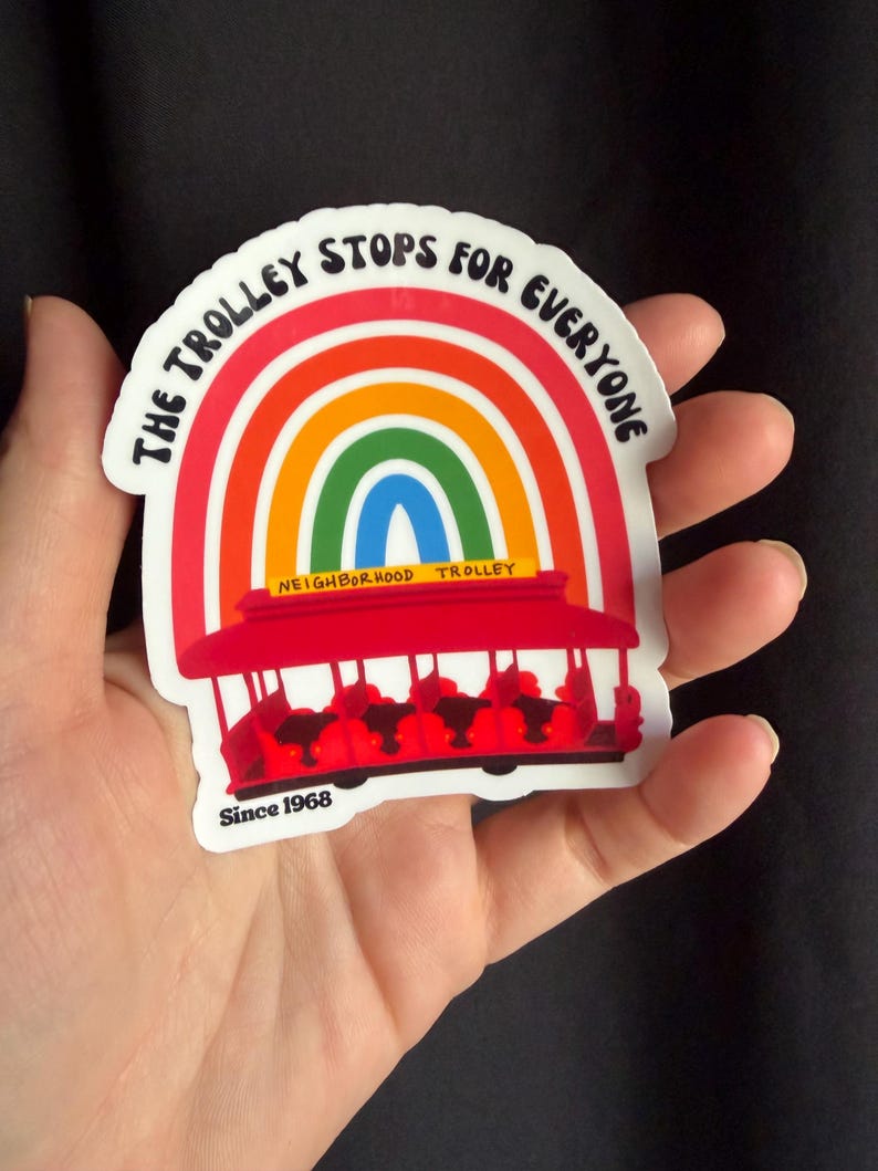 Pu&ograve; includere: Un adesivo raffigurante un tram rosso con un arcobaleno sopra. Il testo "THE TROLLEY STOPS FOR EVERYONE" &egrave; arcuato sopra l'arcobaleno. L'adesivo include anche il testo "NEIGHBORHOOD TROLLEY" e "Since 1968".