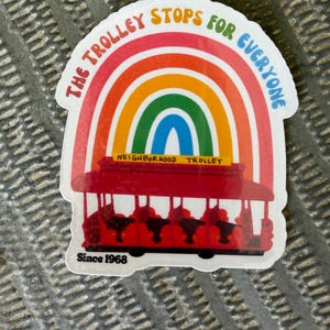 May include: A vibrant sticker with a red trolley design under a rainbow. The text "THE TROLLEY STOPS FOR EVERYONE" is above the rainbow. "NEIGHBORHOOD TROLLEY" is below, and "Since 1968" is at the bottom. A cheerful, colourful design.