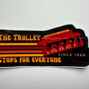Puede incluir: Una pegatina con fondo negro y las palabras "The Trolley Stops For Everyone" en naranja y amarillo. Un gr&aacute;fico de tranv&iacute;a rojo est&aacute; a la derecha, con el texto "Neighborhood Trolley" encima. La pegatina dice "Since 1968".