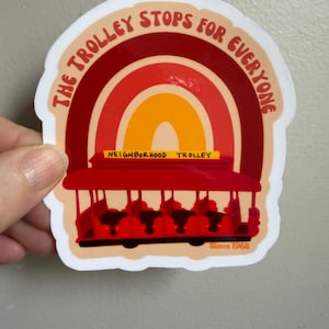May include: A sticker featuring a red trolley with a rainbow design. The text "THE TROLLEY STOPS FOR EVERYONE" arches above the trolley, with "NEIGHBORHOOD TROLLEY" and "Since 1968" displayed below. The sticker has a white border.