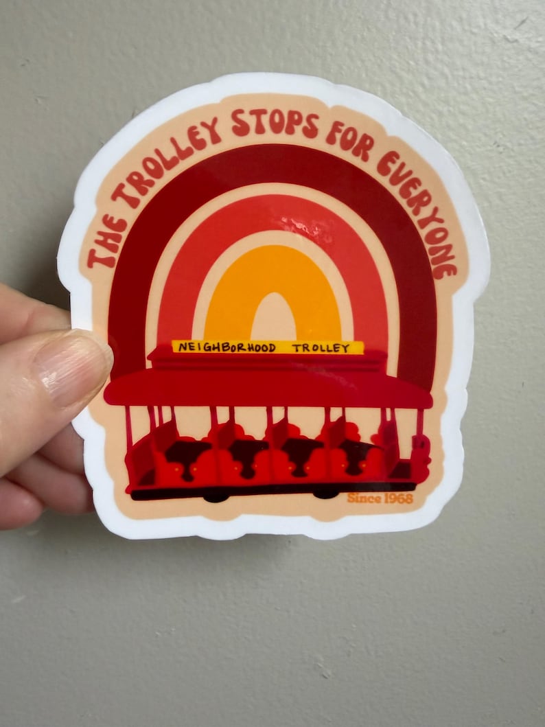 May include: A sticker featuring a red trolley with a rainbow design. The text "THE TROLLEY STOPS FOR EVERYONE" arches above the trolley, with "NEIGHBORHOOD TROLLEY" and "Since 1968" displayed below. The sticker has a white border.