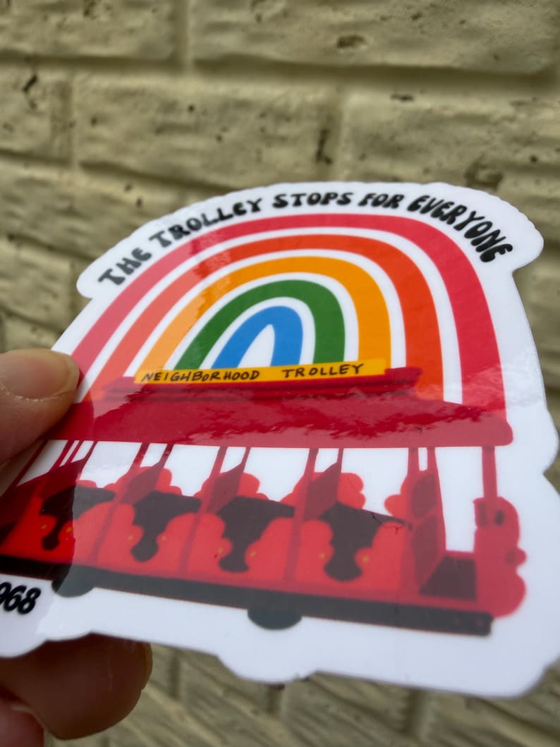 Pu&ograve; includere: Un adesivo raffigurante un tram rosso sotto un arcobaleno, con la scritta "THE TROLLEY STOPS FOR EVERYONE". Il tram ha sedili neri ed &egrave; etichettato "NEIGHBORHOOD TROLLEY" in giallo. L'adesivo ha un bordo bianco.