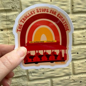 May include: A sticker with a red trolley illustration and the text "The Trolley Stops For Everyone." The design includes a rainbow arch and the words "Neighborhood Trolley" and "Since 1968."