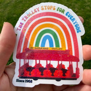 May include: A vibrant sticker depicting a red trolley beneath a rainbow, with the words "THE TROLLEY STOPS FOR EVERYONE" and "NEIGHBORHOOD TROLLEY". The sticker also includes "Since 1968".