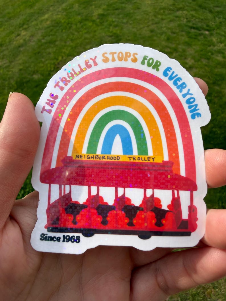 May include: A vibrant sticker depicting a red trolley beneath a rainbow, with the words "THE TROLLEY STOPS FOR EVERYONE" and "NEIGHBORHOOD TROLLEY". The sticker also includes "Since 1968".