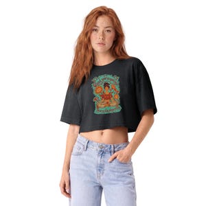 May include: A charcoal gray cropped t-shirt featuring a central graphic of a person meditating in a lotus position surrounded by sunflowers and birds. The text "Feed your empathy, starve the algorithm" is printed in a teal script font.