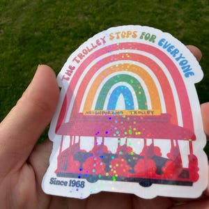 May include: A sticker with a rainbow design above a red trolley illustration. The text reads "THE TROLLEY STOPS FOR EVERYONE" and "NEIGHBORHOOD TROLLEY". The sticker also includes the text "Since 1968".