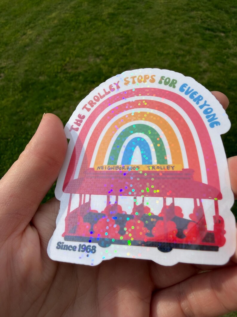 May include: A sticker with a rainbow design above a red trolley illustration. The text reads "THE TROLLEY STOPS FOR EVERYONE" and "NEIGHBORHOOD TROLLEY". The sticker also includes the text "Since 1968".