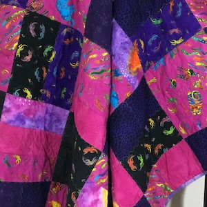 May include: A colorful quilt with a patchwork design featuring pink, purple, and black fabric. The quilt is made up of squares with different patterns, including a floral design and a geometric design.
