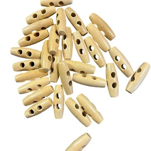 Könnte beinhalten: Ein Haufen von 20 natürlichen Holz-Toggle-Knöpfen mit jeweils zwei Löchern. Die Knöpfe sind oval geformt und haben eine glatte, unbehandelte Oberfläche.