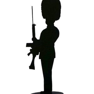 Puede incluir: Silueta negra de un guardia real británico con rifle y sombrero de piel de oso. La figura está montada sobre una base circular, representando un elemento decorativo y simbólico.