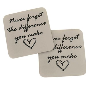 May include: Two square coasters with rounded corners. Each coaster features the phrase "Never forget the difference you make" in black script, with a hand-drawn heart below. The coasters are a light, neutral colour.