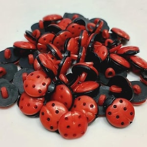 Peut inclure: Une collection de petits boutons ronds en forme de coccinelles. Chaque bouton présente un dessus rouge vif avec des points noirs et une base noire avec une attache centrale. Les boutons sont empilés en un groupe, montrant plusieurs unités.
