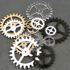 May include: A collection of gears in different sizes and colours, including white, black, clear, and tan. The gears are made from various materials and are arranged together, displaying their intricate designs.