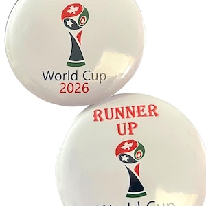 May include: Two round white pinback buttons featuring a graphic of a trophy with a maple leaf and star. One button displays the red text WINNER above the trophy and World Cup 2026 below. The other button displays RUNNER UP in red text.