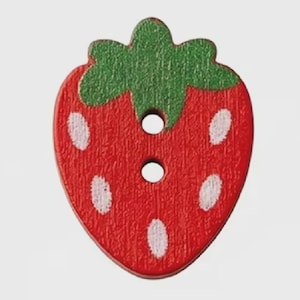 May include: A strawberry-shaped button with a red body, a green stem at the top, and white seed-like markings. The button features a textured surface and two circular holes positioned vertically in the centre for attachment to fabric.