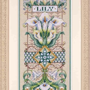 Op de afbeelding: Een ingelijst borduurwerk met kruissteek, met een witte lelie met groene bladeren en een decoratieve rand. Het woord "LILY" is in het midden van het ontwerp geborduurd.