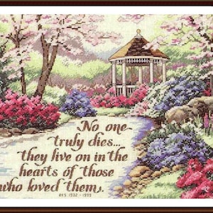May include: Cross-stitch artwork depicting a serene garden scene with a gazebo, lush flowers, and a winding path. The artwork features the text "No one truly dies... they live on in the hearts of those who loved them." The piece is framed in a dark brown wooden frame.