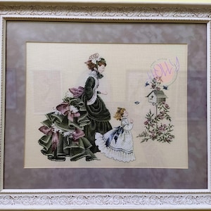 Può includere: Un ricamo a punto croce incorniciato che raffigura due donne in abiti d'epoca vittoriana. La donna in primo piano indossa un vestito verde con un grande fiocco e guarda una casetta per uccelli. La donna sullo sfondo indossa un vestito verde con un grande fiocco e guarda la donna in primo piano. Lo sfondo è di colore beige chiaro con una casetta per uccelli e uccelli.