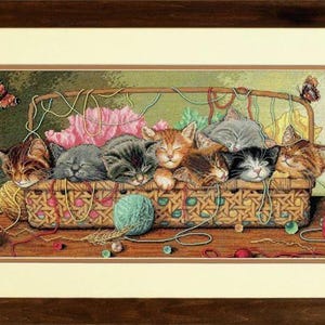 Puede incluir: Una cesta llena de siete gatitos durmiendo, rodeados de hilo de colores y mariposas. Los gatitos están acurrucados juntos en una cesta tejida acogedora.