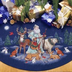 Puede incluir: Una falda de árbol de Navidad azul con una figura de Papá Noel rodeada de animales del bosque, incluyendo un ciervo, un oso y un zorro. La escena se desarrolla en un cielo nocturno estrellado.
