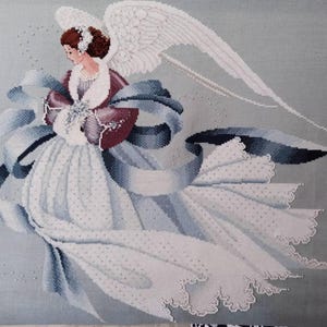 Può includere: Un'immagine a punto croce di un angelo con ali bianche e un abito bianco fluente. L'angelo presenta un motivo floreale bordeaux e bianco e un nastro blu. Lo sfondo è grigio tenue.