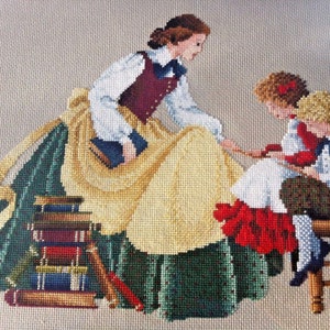 Può includere: Una donna con un vestito verde e giallo legge a due bambini seduti su uno sgabello. La donna tiene un libro e i bambini ascoltano attentamente. La scena è ricamata con filo colorato.
